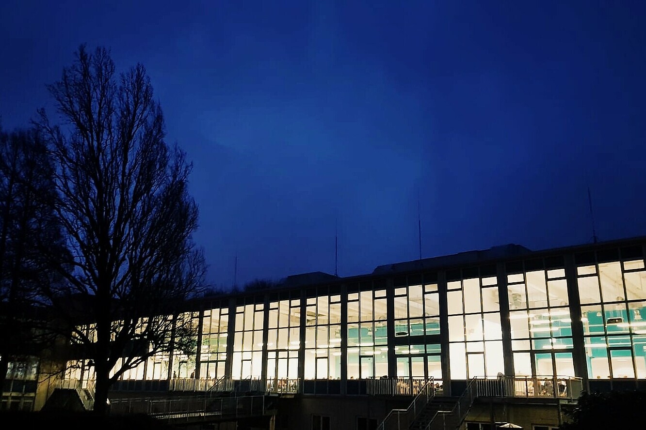 Gebäude C auf dem Campus Eupener Straße ist hell erleuchtet und setzt sich vom dunkelblauen Himmel ab.